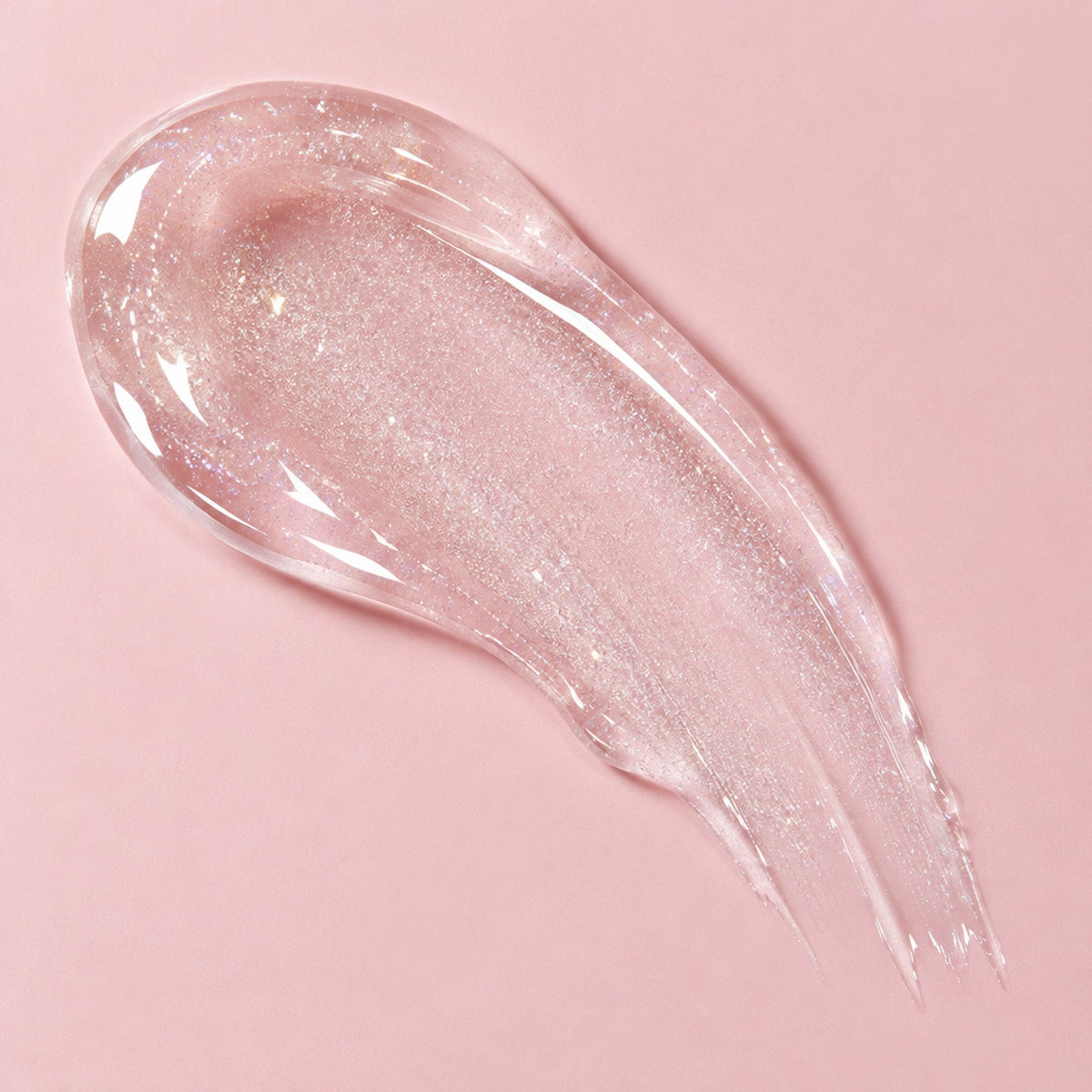 A swatch of clear, shimmery Luma Lips plumping gloss on a pale pink background